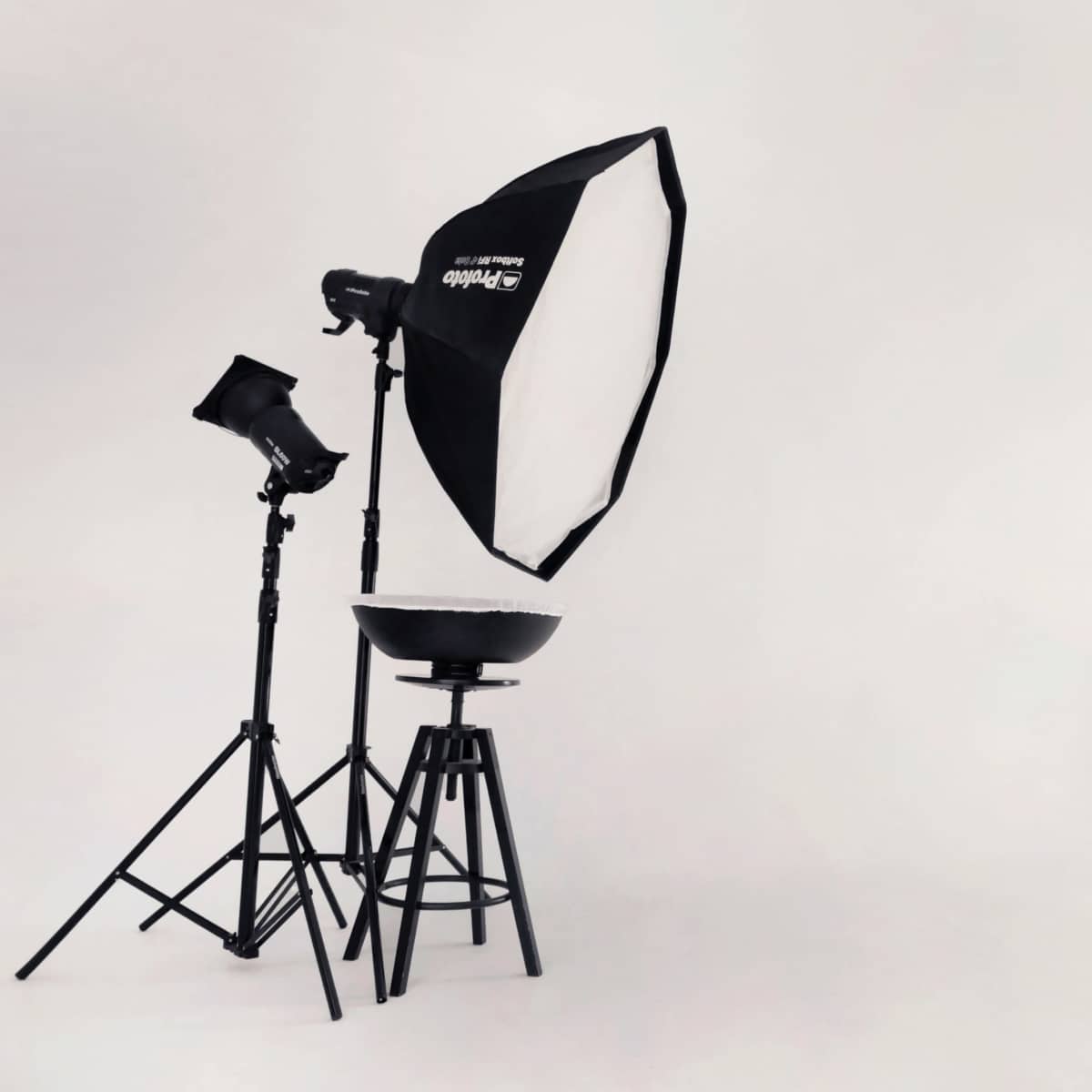 A photography studio with lighting equipment, a black stool, and a rolling cart against a plain white backdrop.