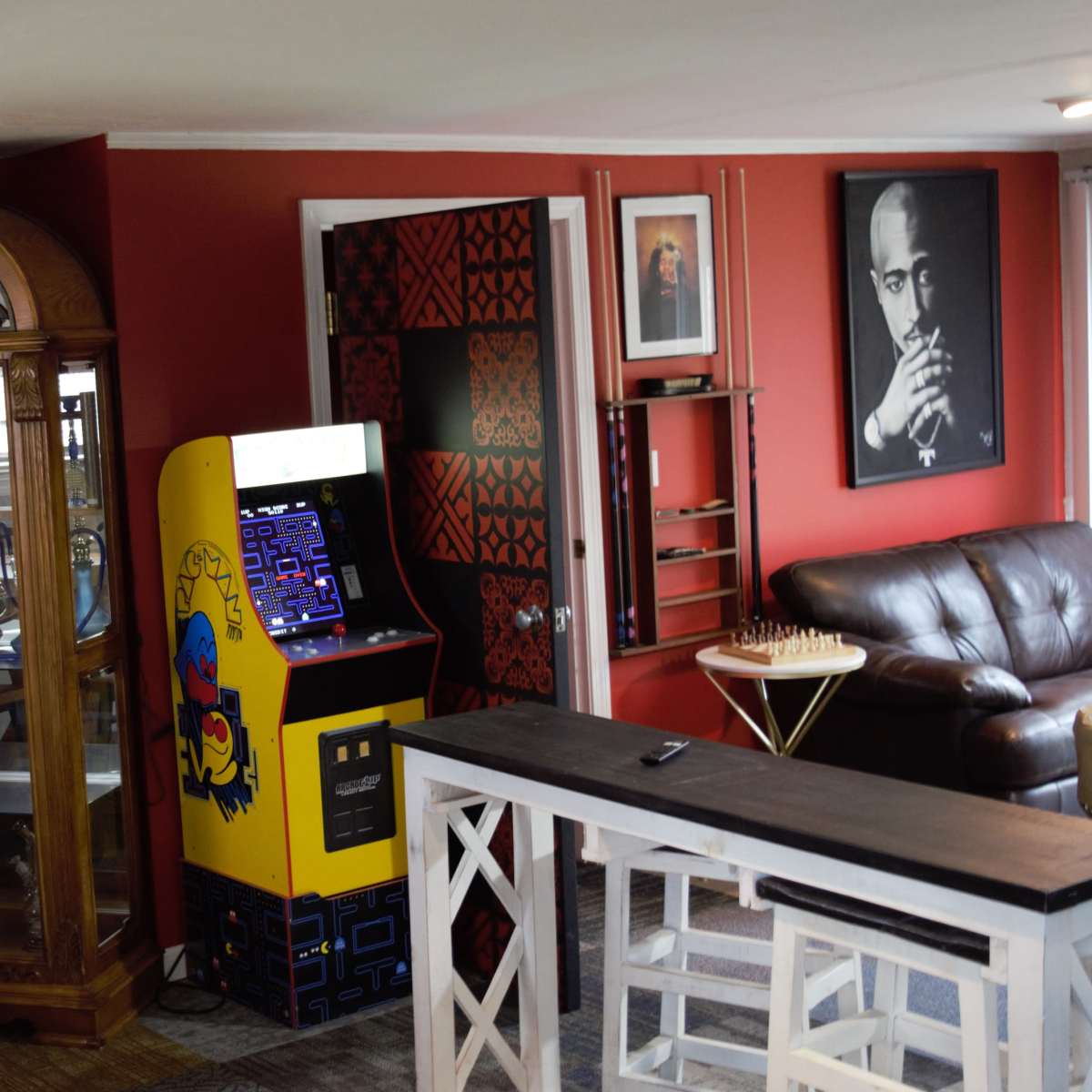 A cozy interior featuring a vintage arcade game, a wooden display cabinet, and various artworks on the walls.