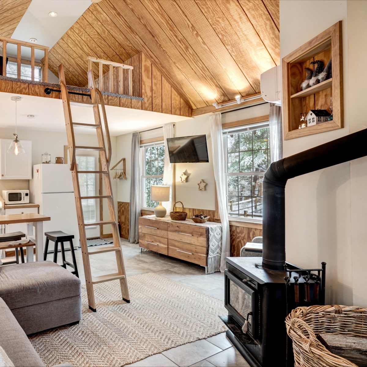 A modern, open-concept living space with a high wooden ceiling, a lofted area, and a cozy seating arrangement near a wood-burning stove.