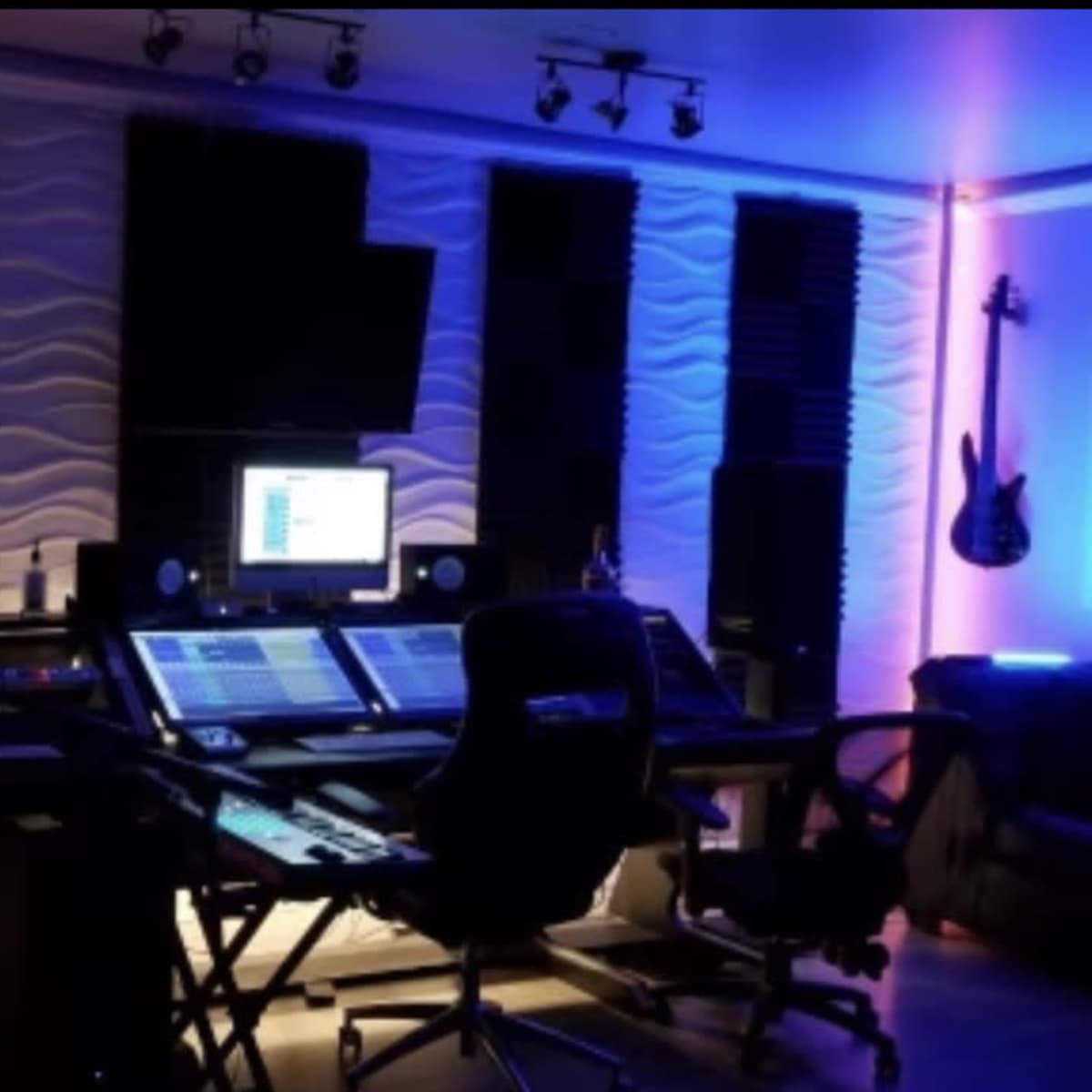 A music production studio with soundproof walls, a control desk equipped with audio equipment, and soft, colored lighting.