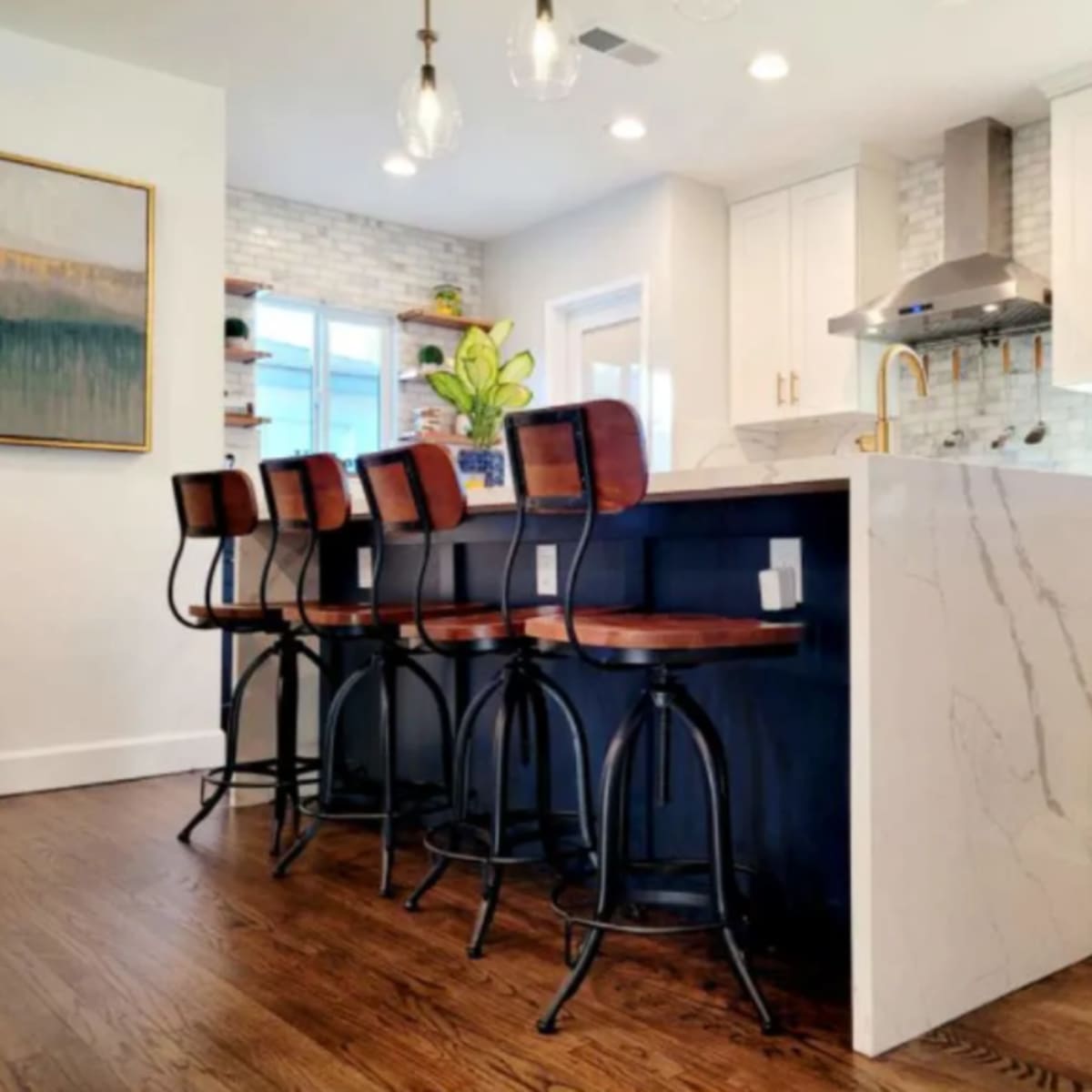 A modern kitchen with a large island featuring swivel bar stools, white cabinetry, and a stone backsplash.