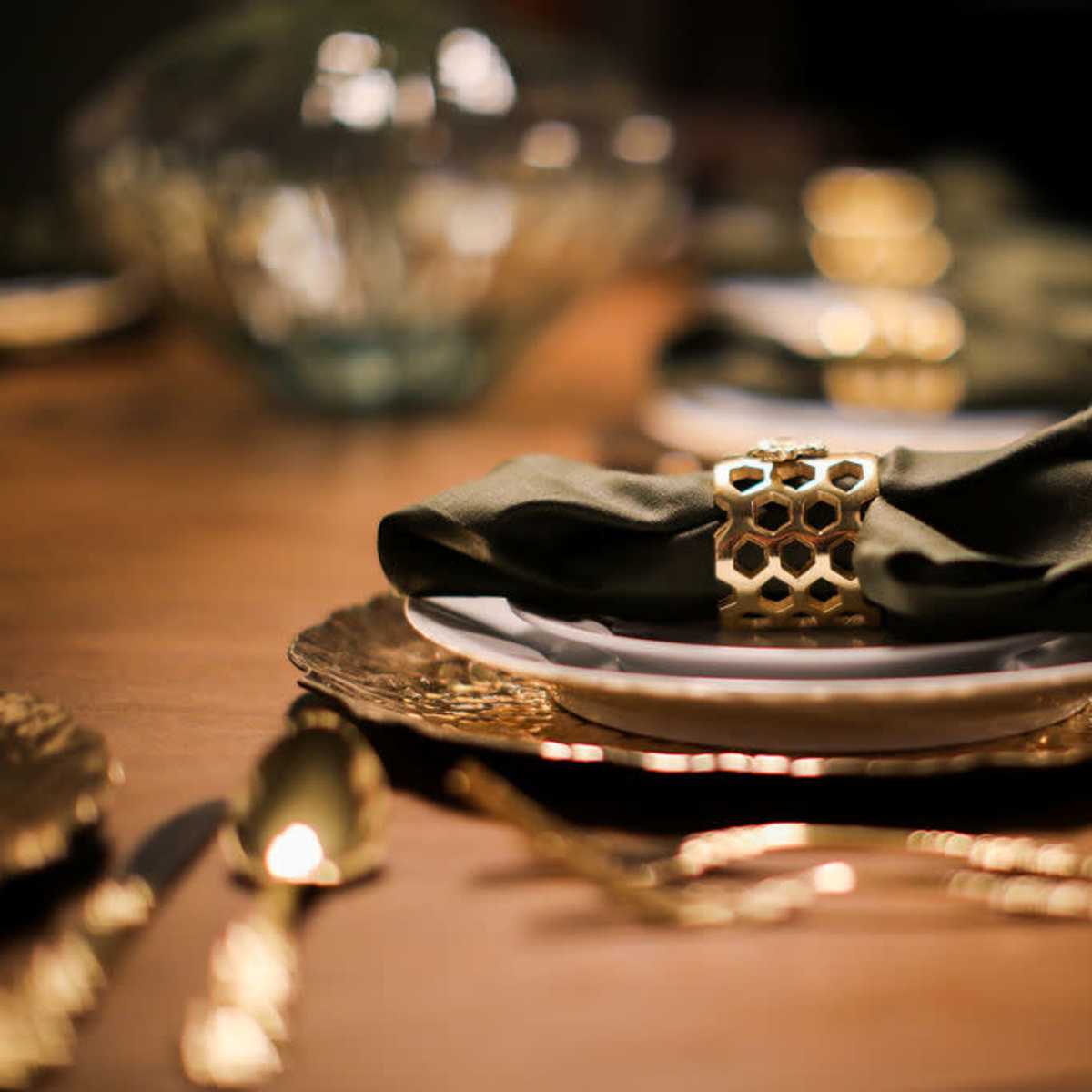 A beautifully set dining table features plates with green napkins secured by decorative gold rings, surrounded by elegant cutlery.