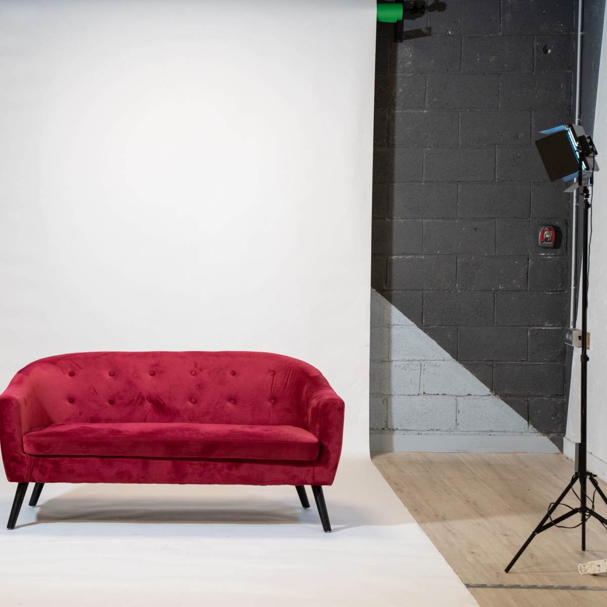 A red velvet sofa is centered in a photography studio with a white backdrop and two lighting setups on either side.