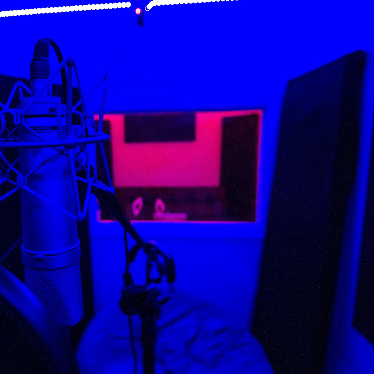 A recording studio with a microphone positioned in the foreground and soundproof panels in the background, illuminated by blue and red lights.