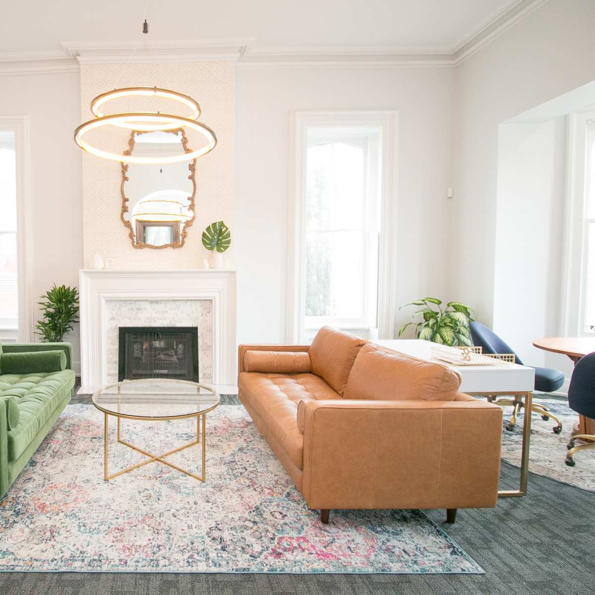 A brightly lit room furnished with a green sofa, a brown leather sofa, a circular coffee table, and a decorative fireplace.
