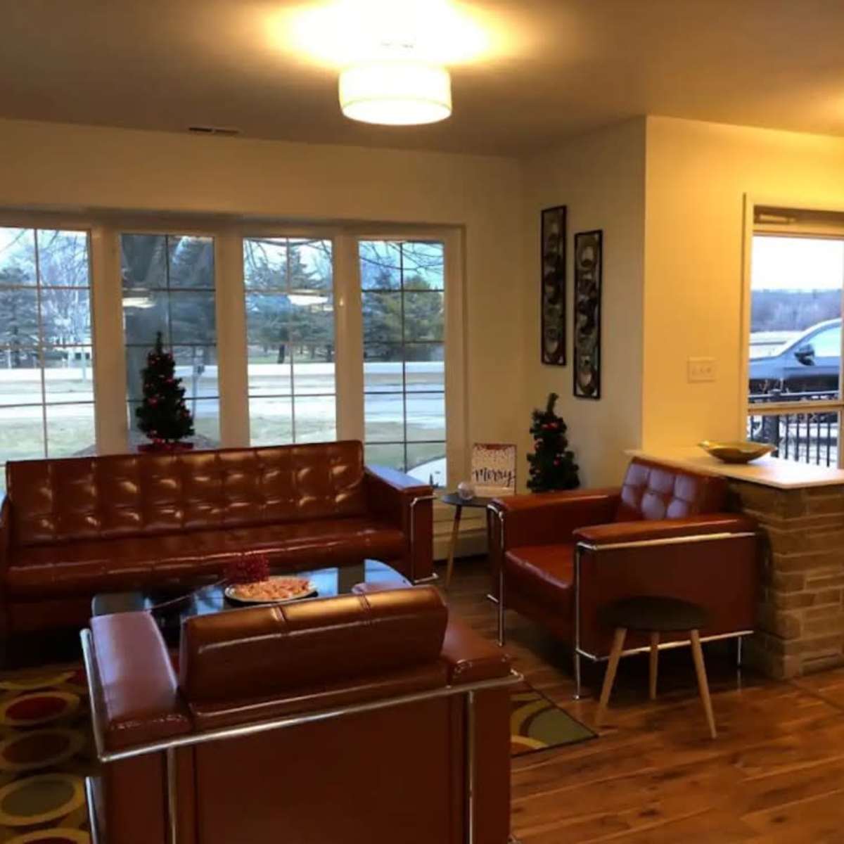 A living room with brown leather furniture, a coffee table, two small Christmas trees, and a door leading outside.