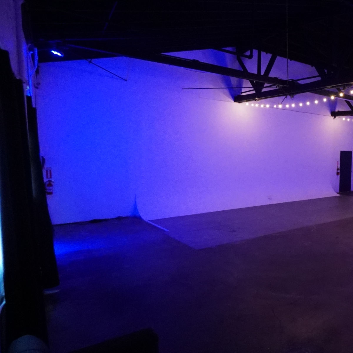 A spacious room with exposed beams, featuring blue ambient lighting and a concrete floor.