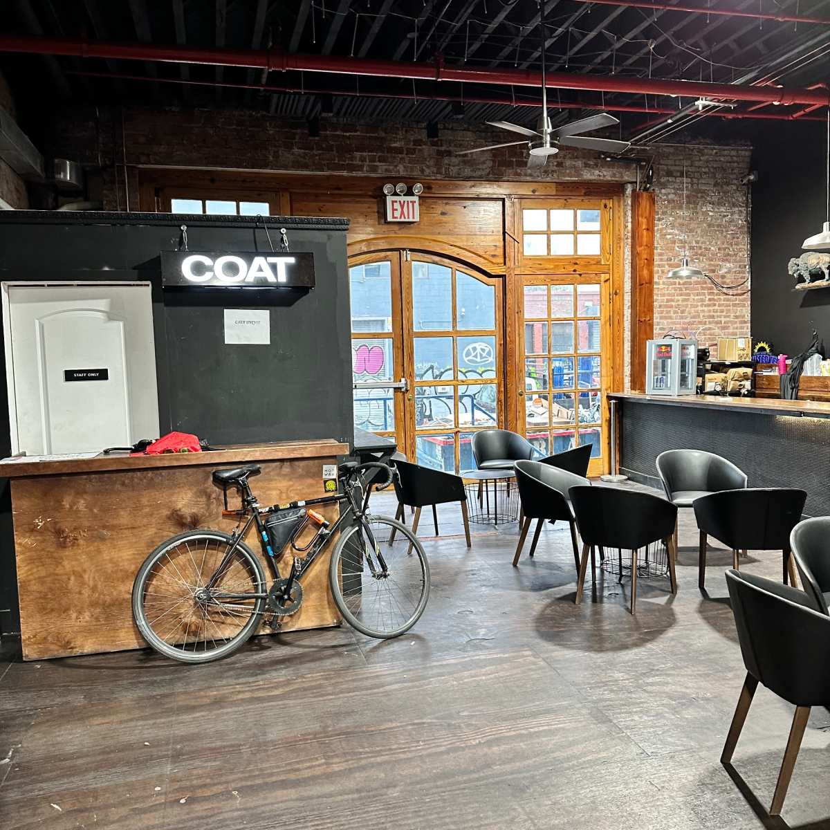 A bicycle leans against the wooden counter in a modern café with black chairs and large windows displaying urban art.