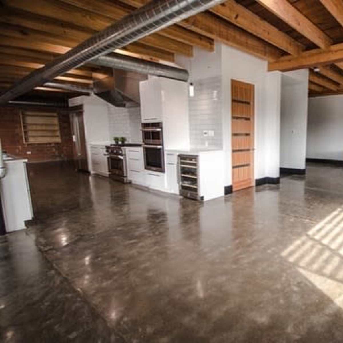 A spacious industrial-style kitchen and living area with polished concrete floors, exposed wooden beams, and minimalistic furnishings.