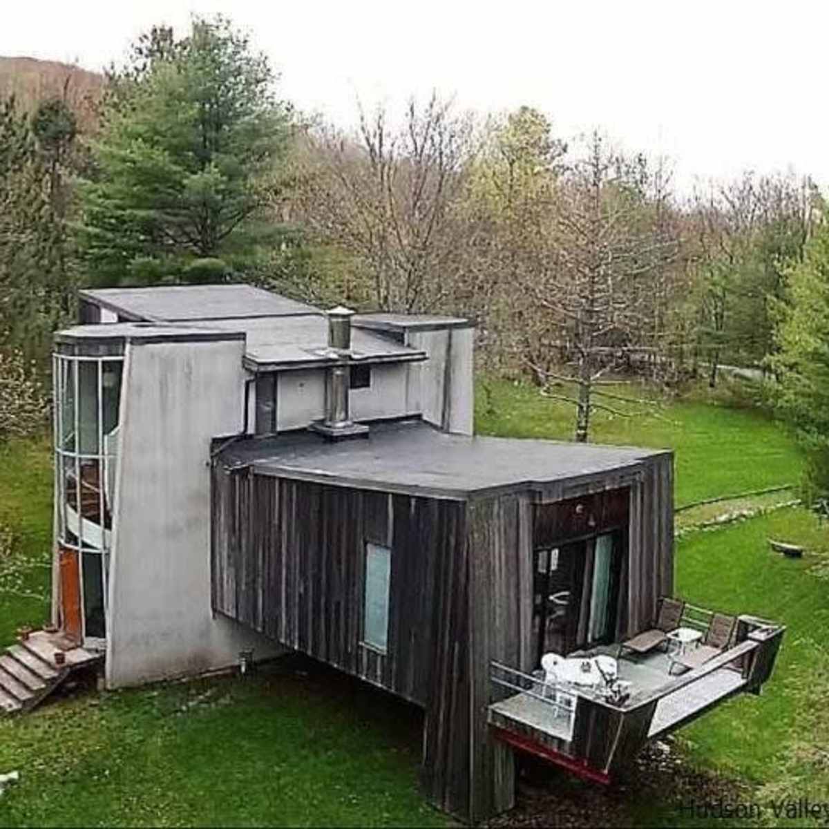 A modern, asymmetrical house with a mix of concrete and wooden exterior is situated in a wooded area.