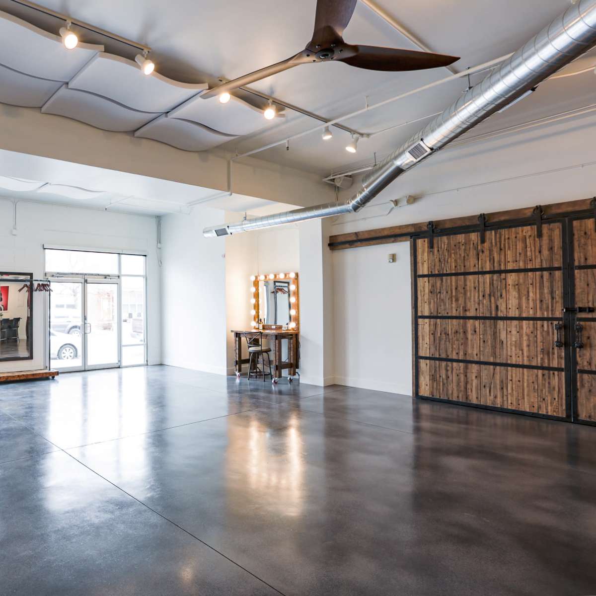 A spacious interior features large windows, polished concrete floors, and a vanity station against a wooden wall.