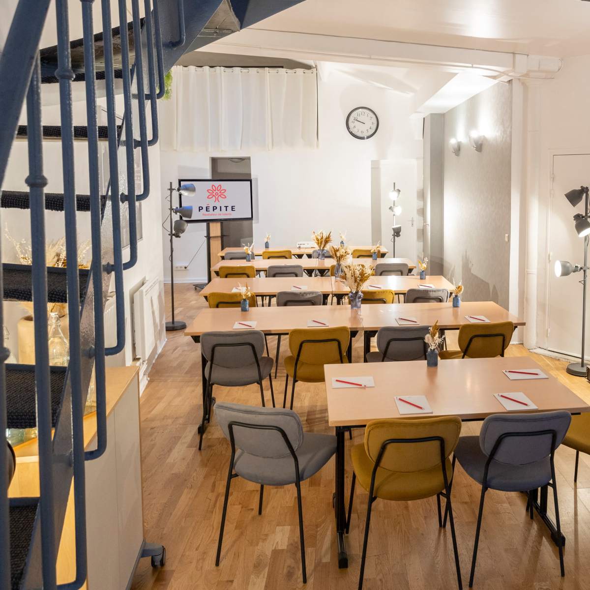 A spacious meeting room features several tables arranged in rows, with chairs and a presentation screen at the front.