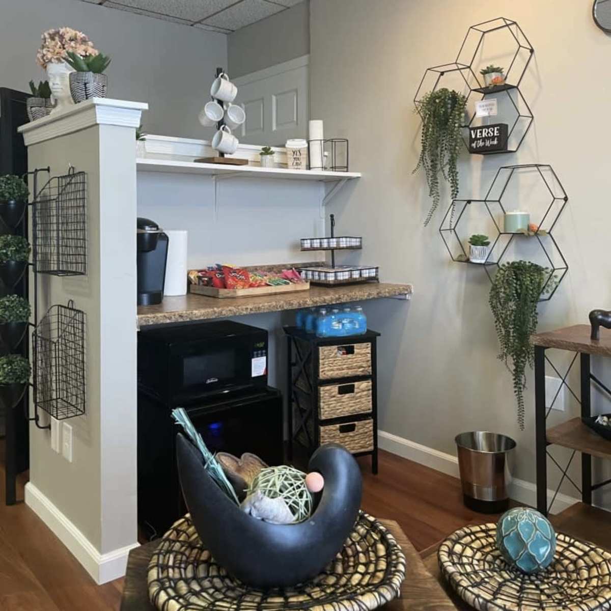 A cozy interior space featuring a small kitchenette area with snacks, a coffee machine, and decorative wall shelves arranged with plants.