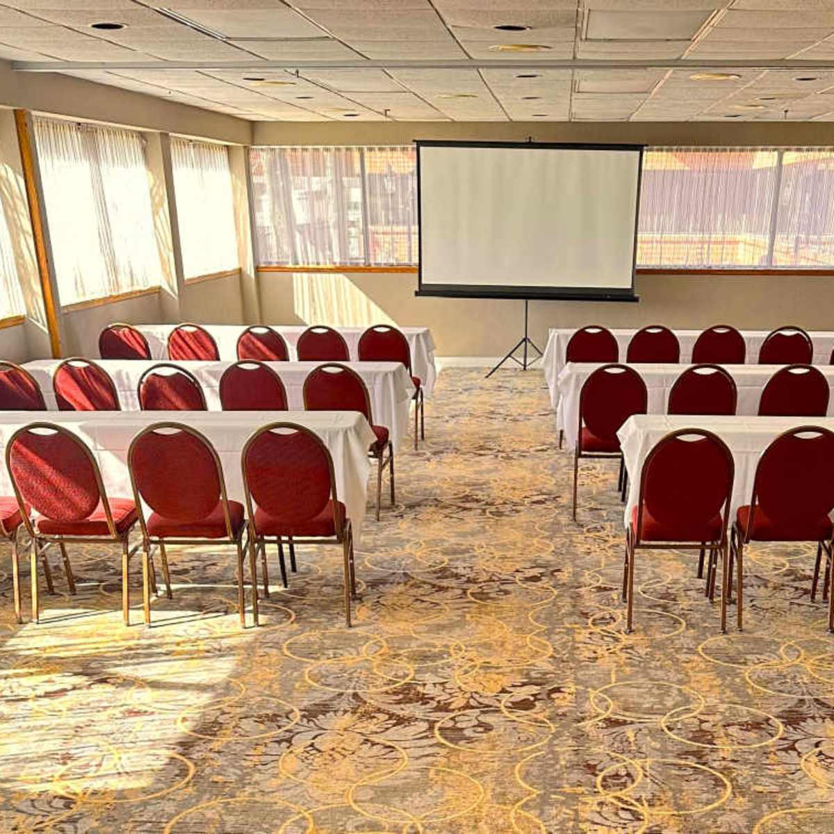 A conference room with rows of red chairs and white tables facing a projection screen.