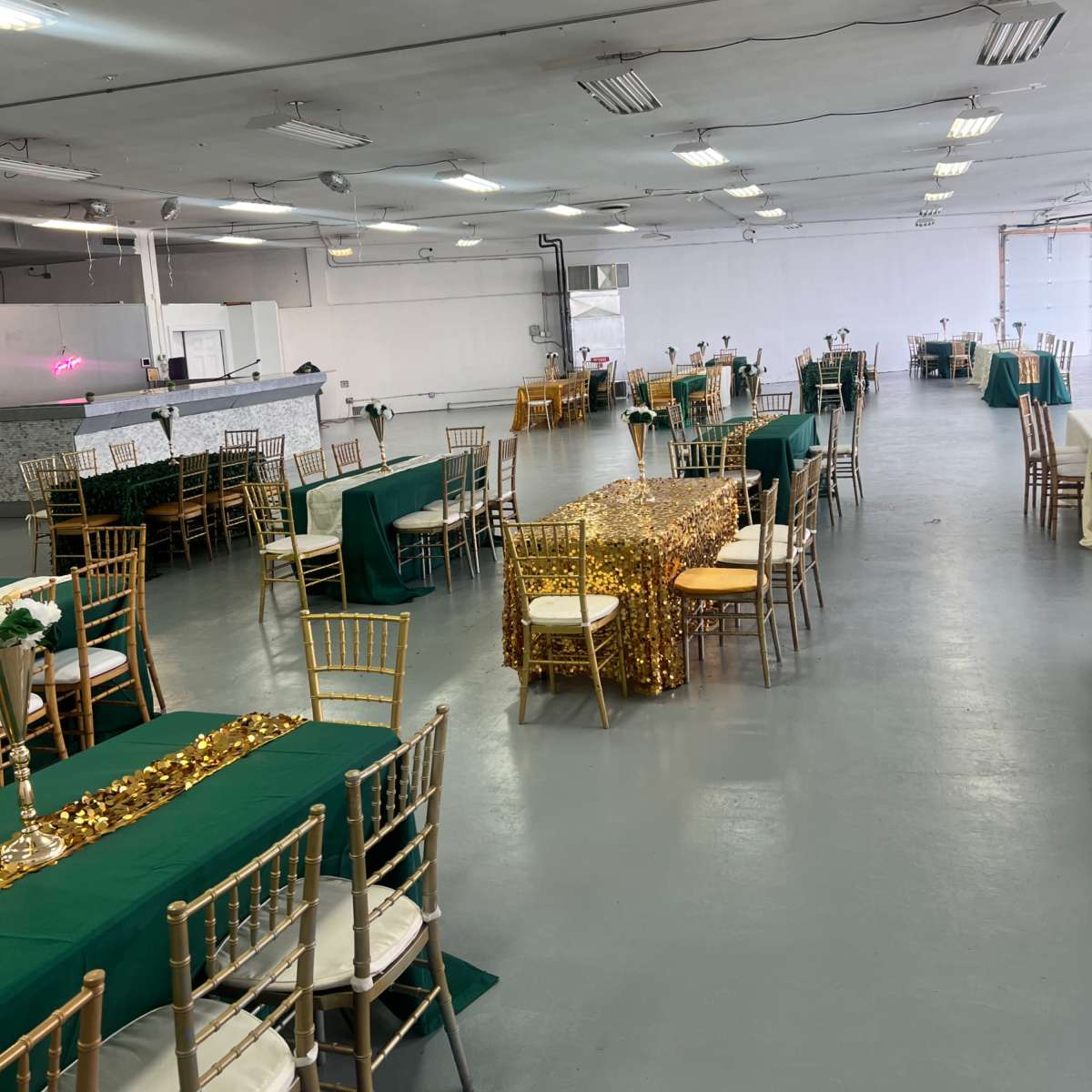 A large event space set up with multiple tables covered in green and gold decorations, arranged in rows.