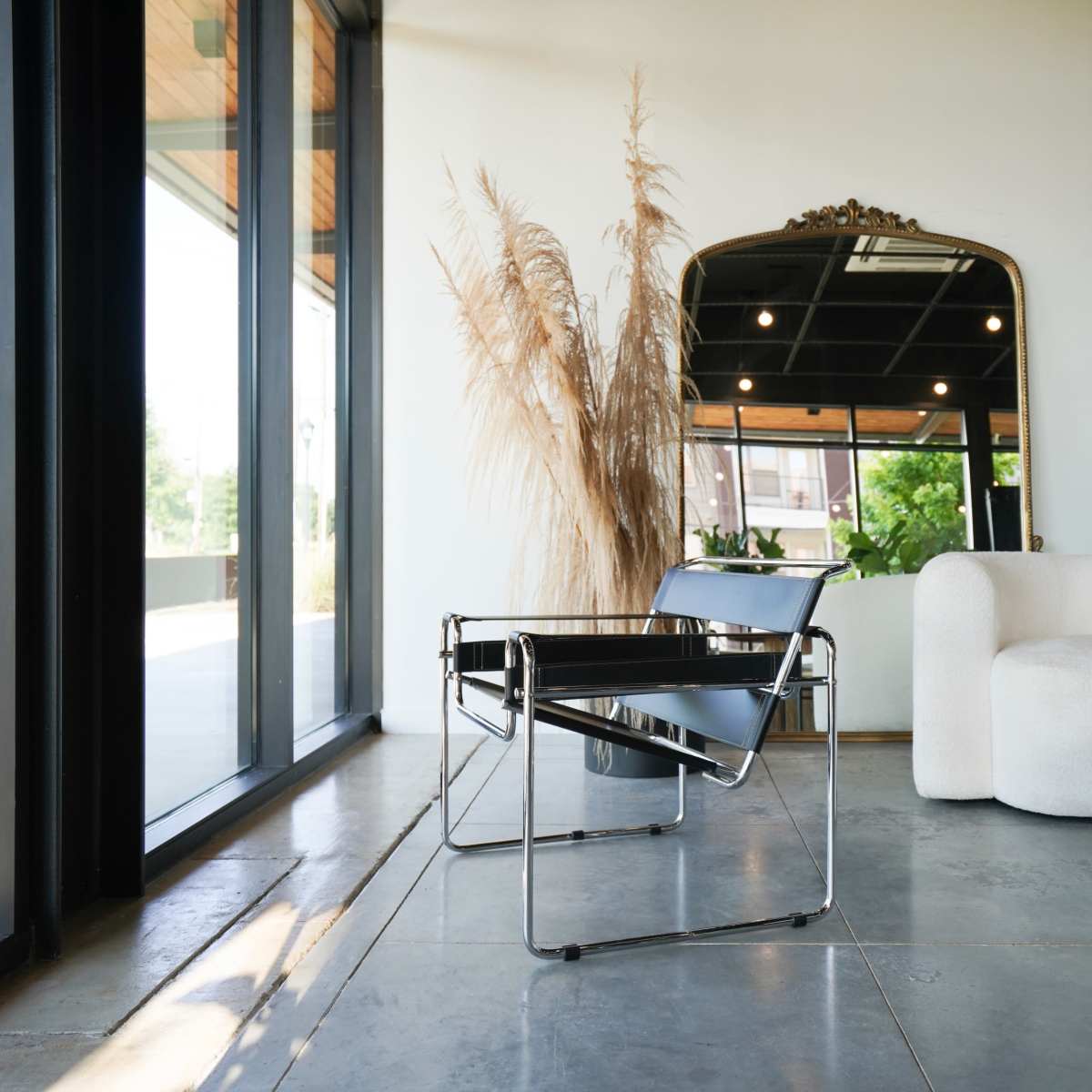 A modern living space featuring a minimalist chair, a round table with a magazine, and large windows allowing natural light to enter.