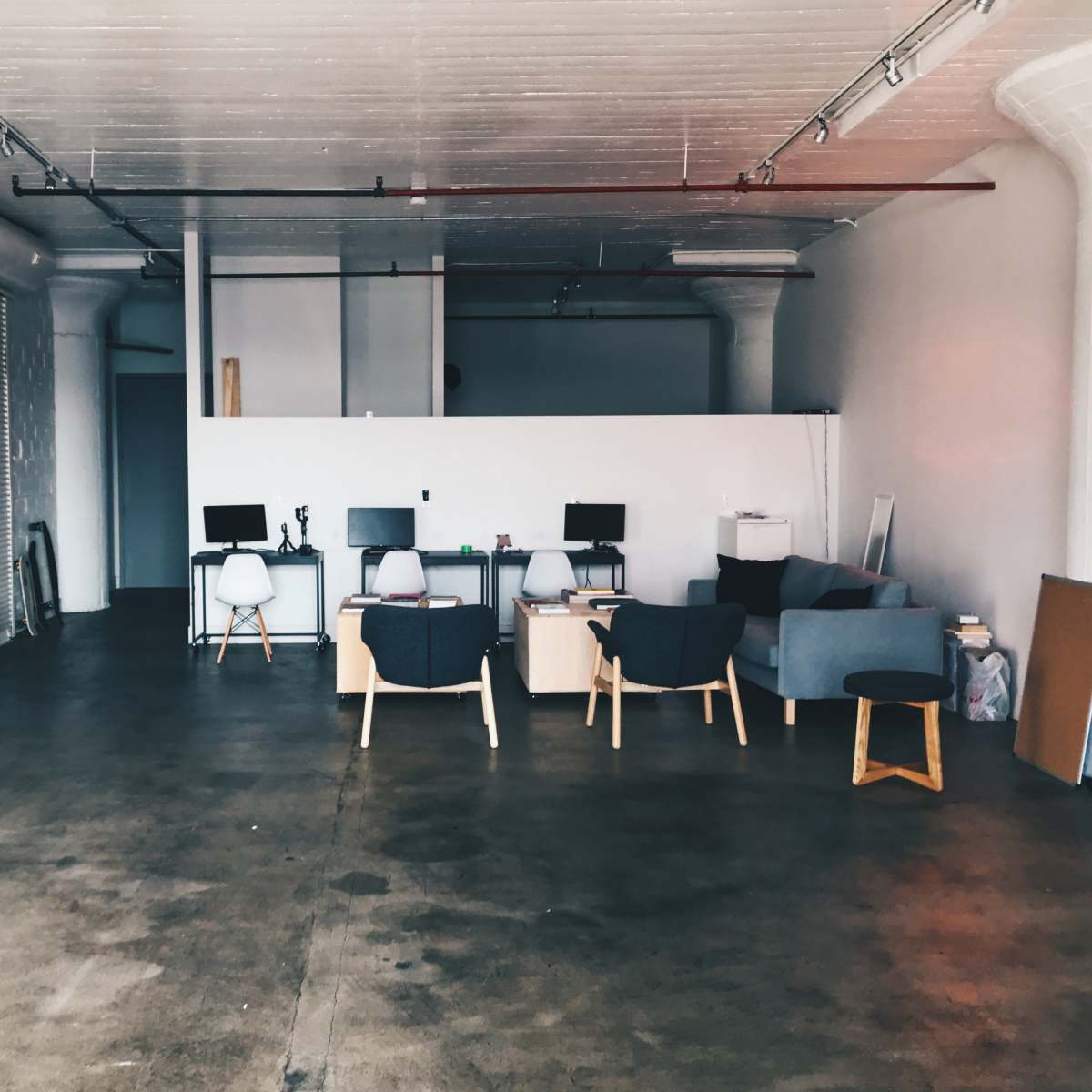 An empty workspace with several desks, chairs, and a small seating area in a well-lit, spacious setting.