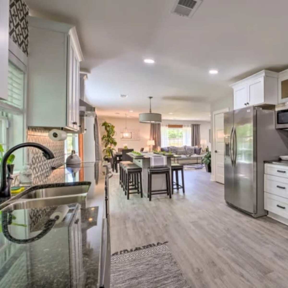 A modern kitchen with white cabinetry, a stainless steel refrigerator, and a view into a dining area and living room beyond.