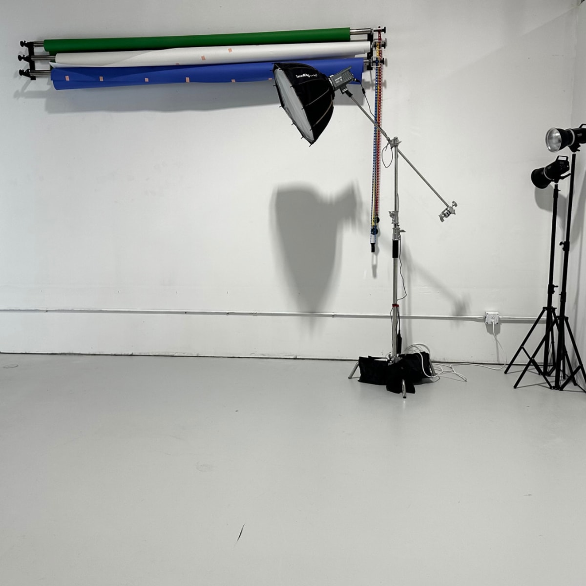 A photography studio with a backdrop system of green and blue rolls, a light setup on a stand, and another light on a tripod.