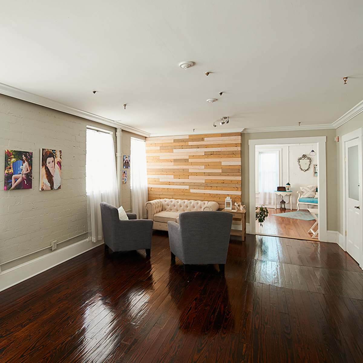 A well-lit room with a cozy seating area featuring two gray chairs and a wall made of wooden panels, accompanied by large windows with sheer curtains.