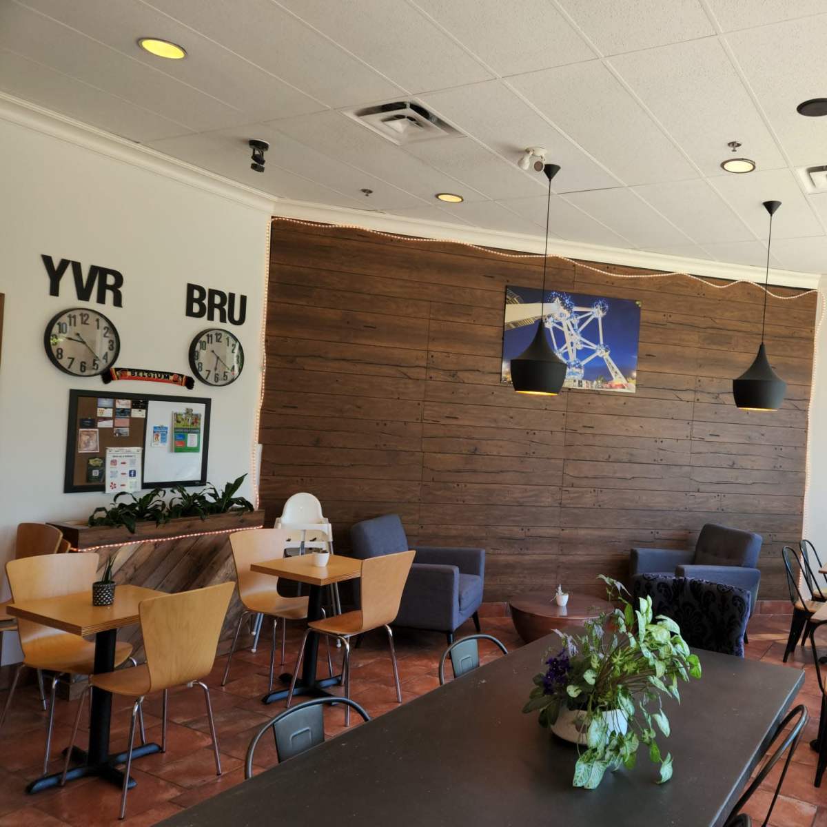 The interior of a cafe features wooden walls, a mix of seating arrangements, and large windows allowing natural light to enter.