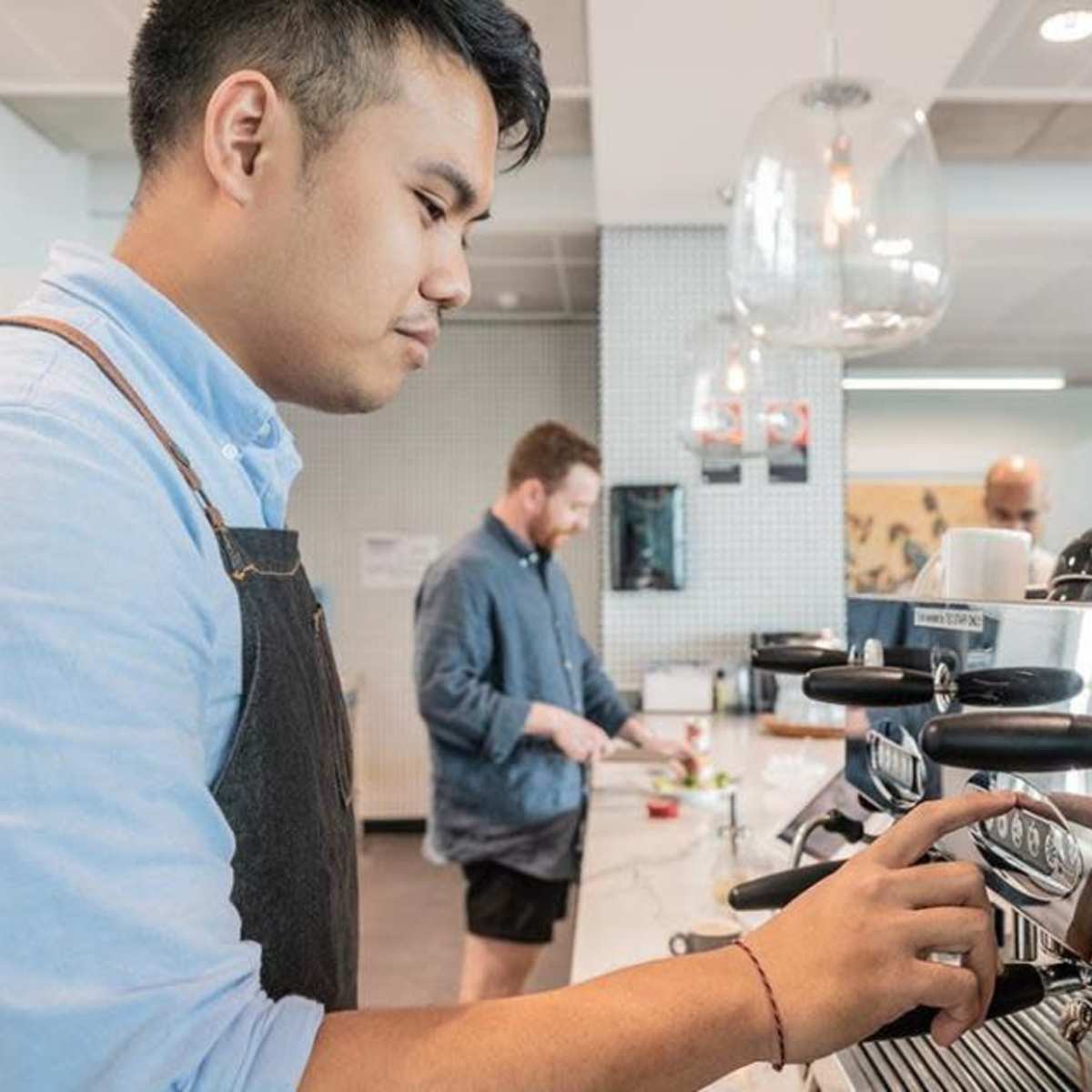 A barista operates an espresso machine while another man prepares coffee in a modern café.