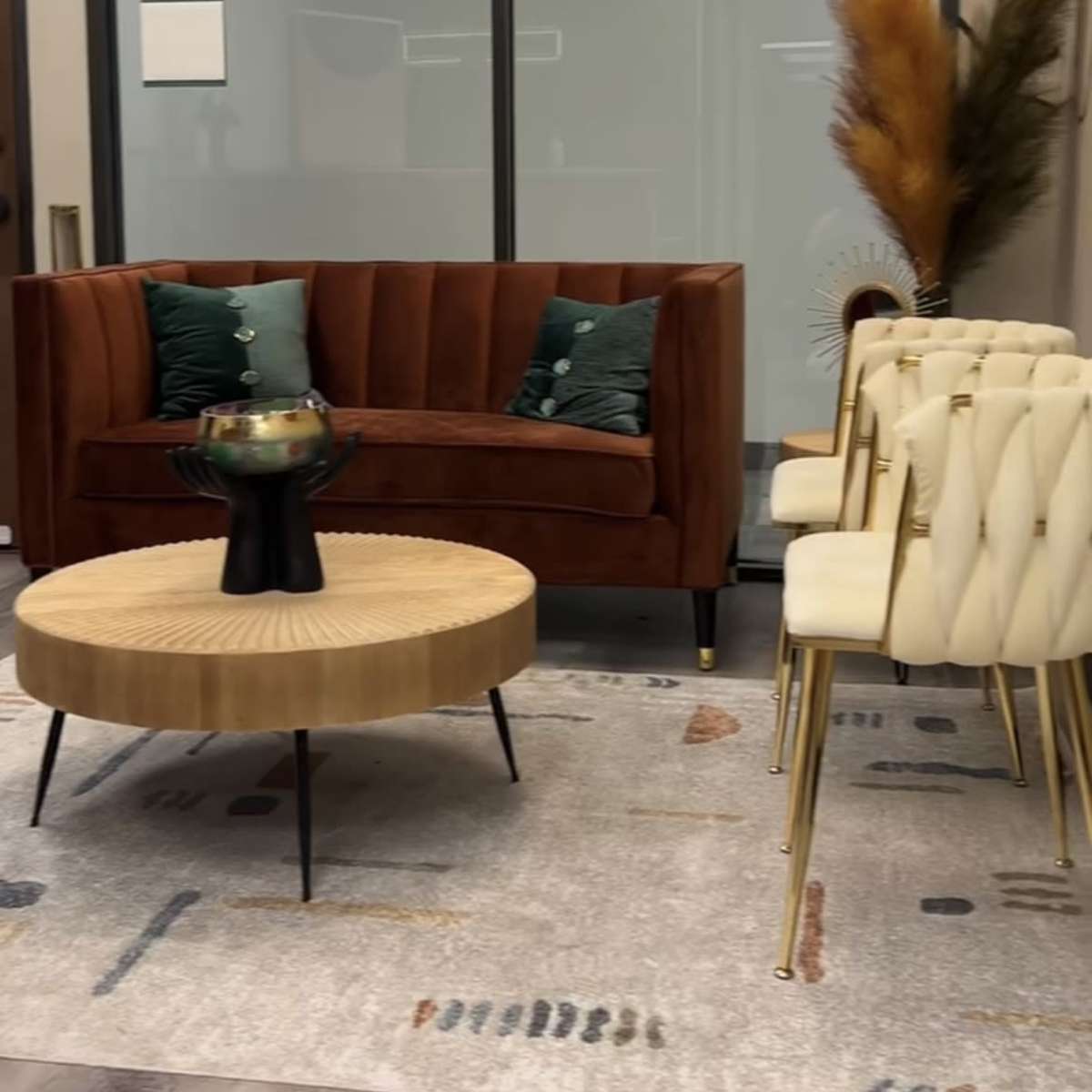 A modern office waiting area features a brown velvet sofa with green cushions, a round wooden coffee table, white upholstered chairs, and decorative plants.