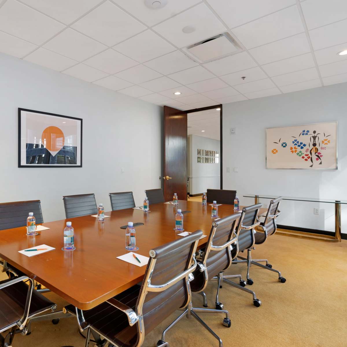 A conference room features a large wooden table surrounded by silver chairs, with water bottles and notepads placed at each seat.