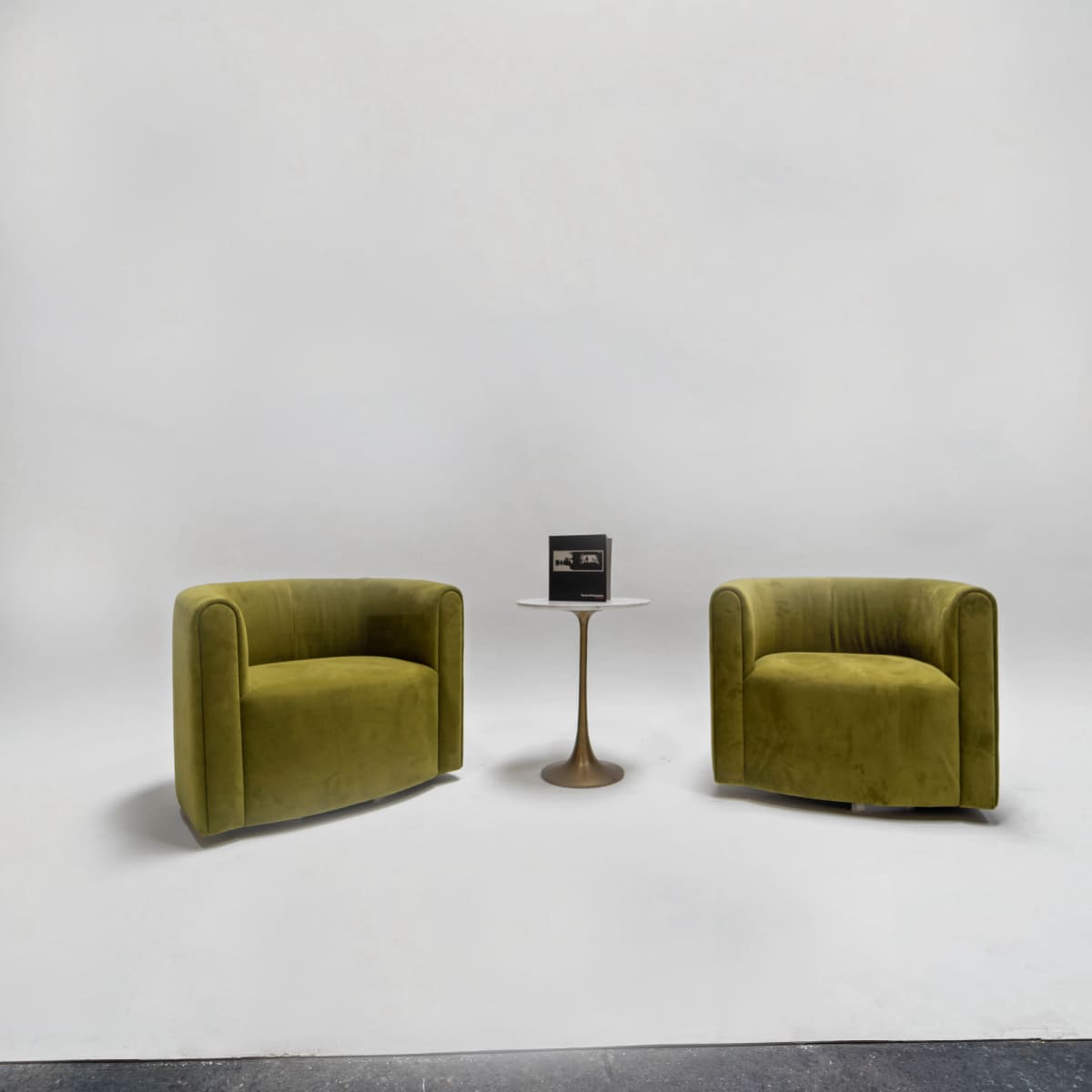 Two green upholstered chairs are positioned opposite each other with a small gold side table in between, set against a neutral backdrop.