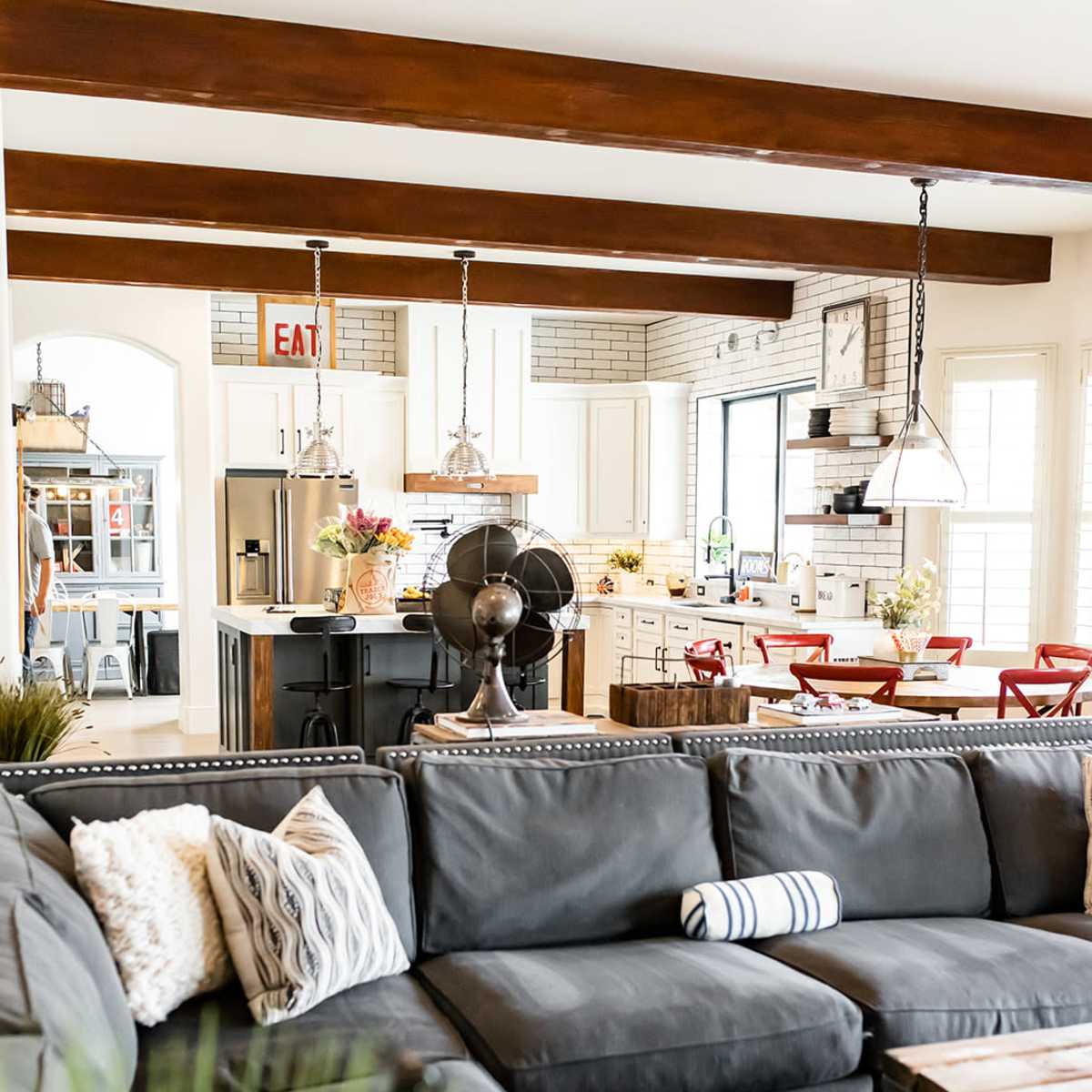 A spacious living room features a gray sectional sofa, a coffee table made of wood, and a view of a modern kitchen in the background.