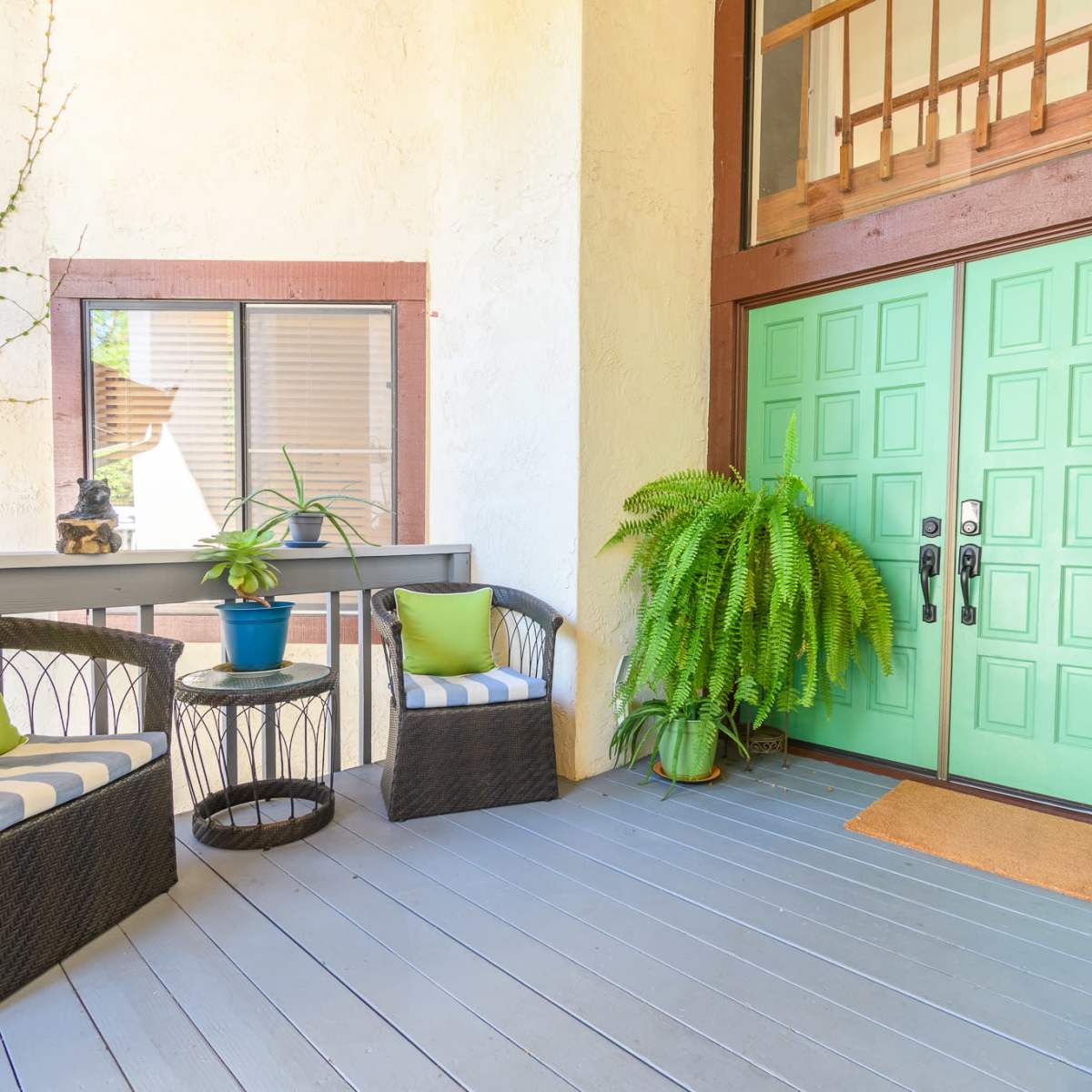 A porch area with two wicker chairs, a small table, potted plants, and a pair of green double doors.