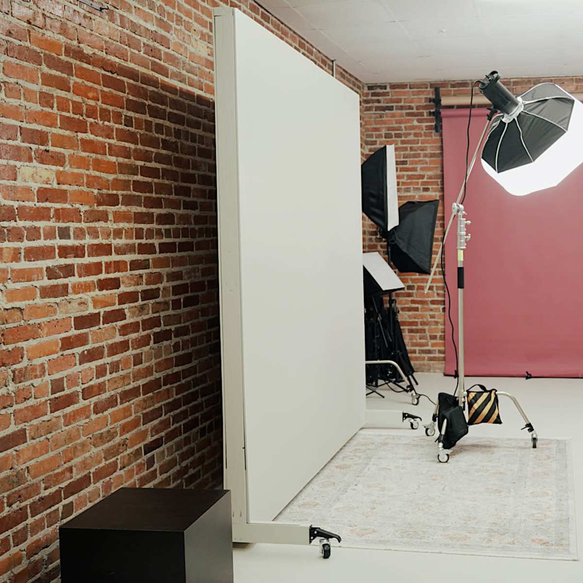 A photography studio with a brick wall, a light setup, a pink backdrop, and a white partition.