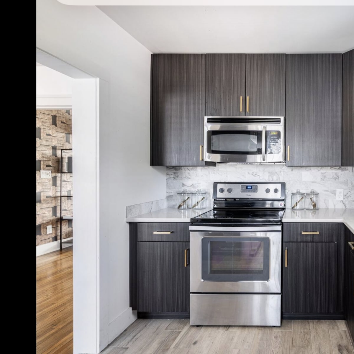 A modern kitchen features dark cabinetry, stainless steel appliances, and a white countertop with a sink and a dish drying rack.