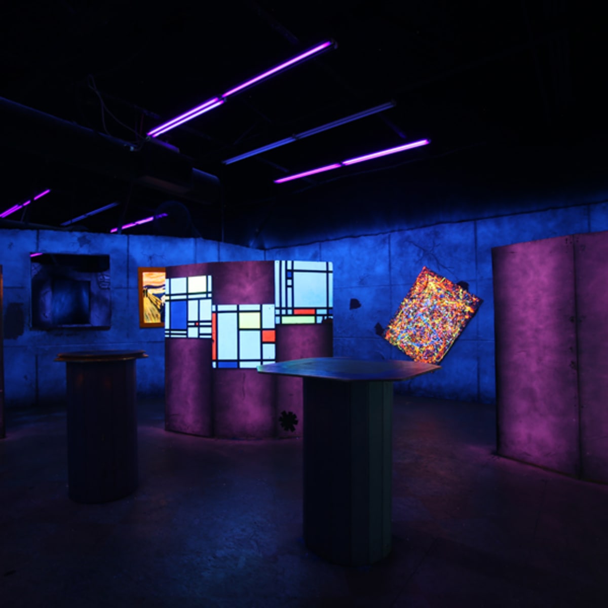 An art installation in a dimly lit room with walls illuminated by purple and blue lights, featuring various abstract displays and columns.