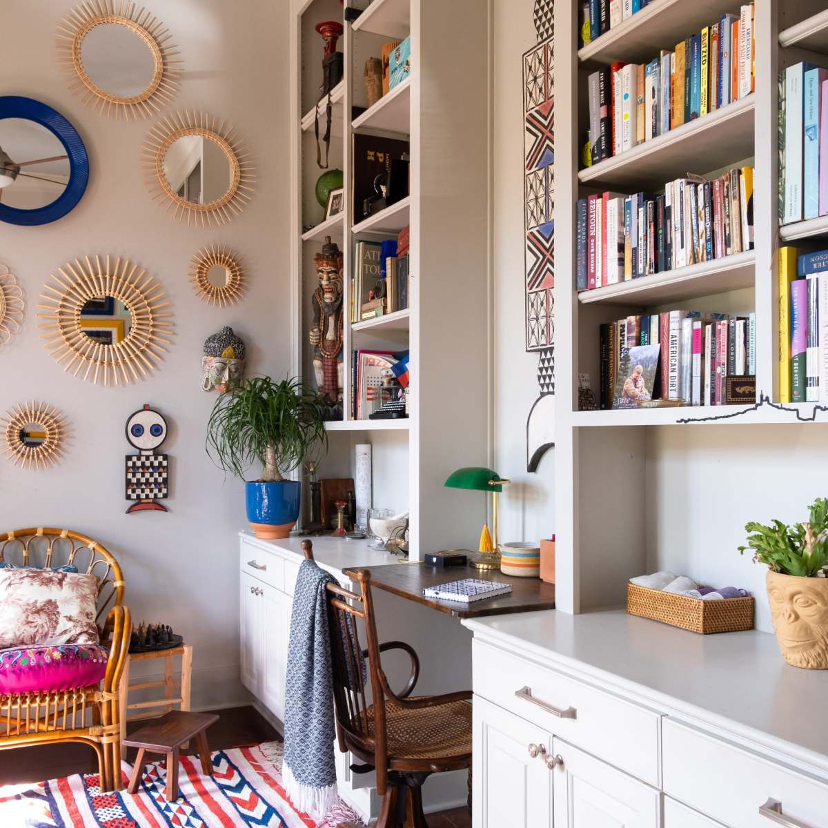A cozy reading nook featuring a bookshelf, decorative mirrors on the wall, a patterned rug, and a desk with a chair.