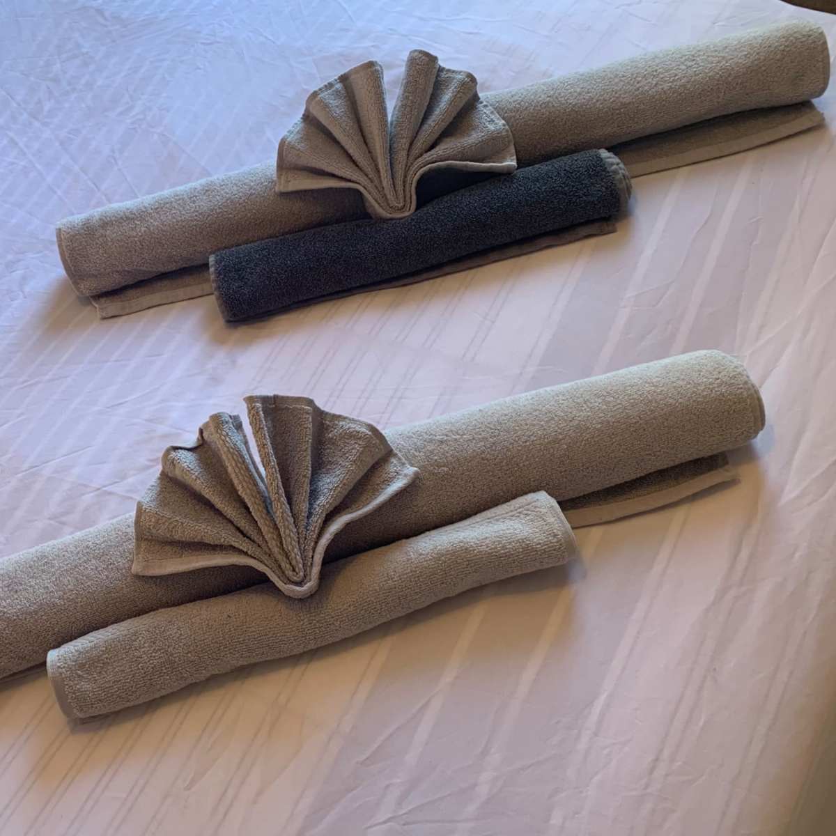 Two rolled towels, decorated with fan-like folds, are arranged neatly on a bedspread.