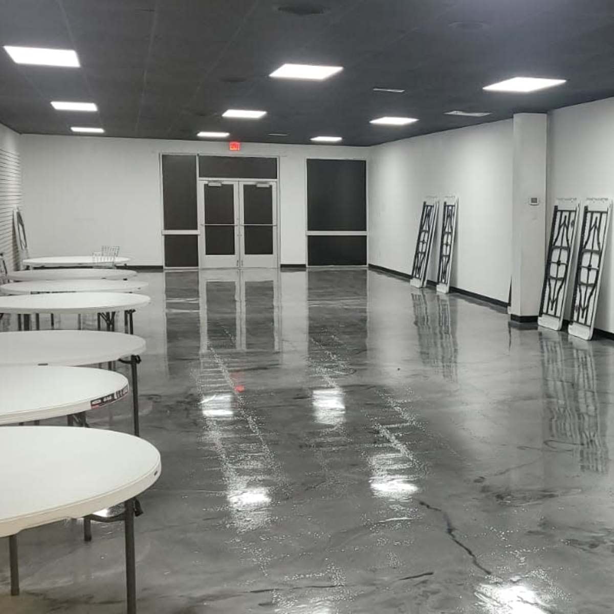A large, empty room with several round tables lined up against the walls and a polished concrete floor.