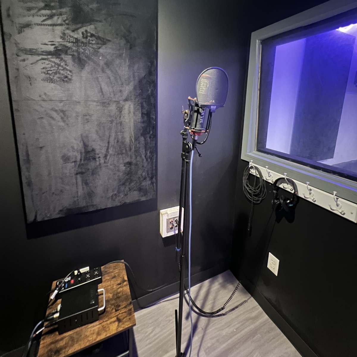 A soundproof recording booth with a microphone on a stand and audio equipment on a wooden table.