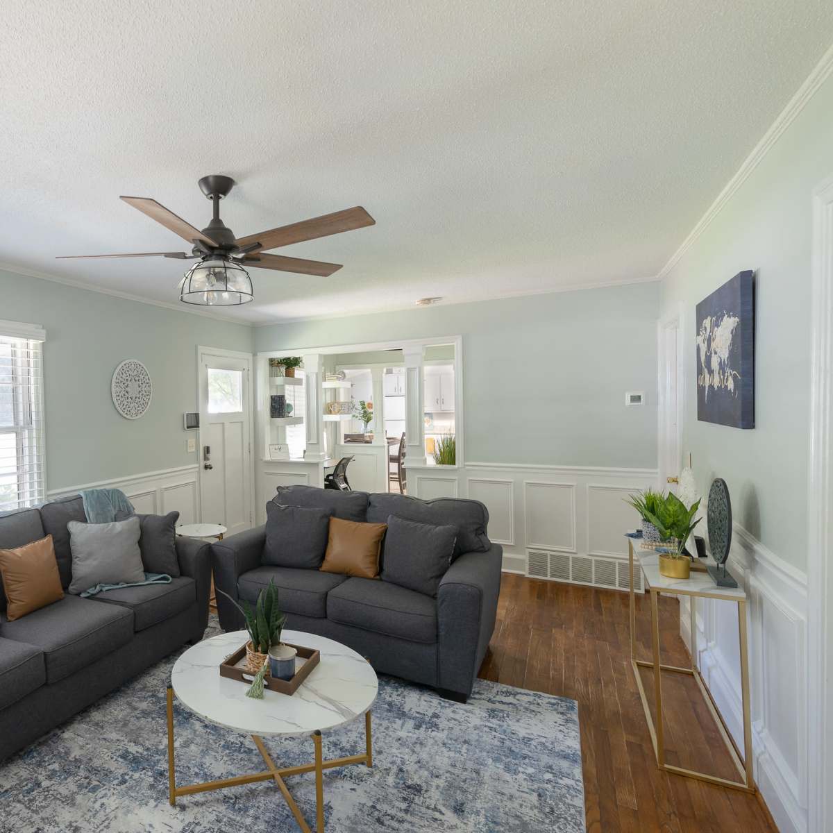 A living room with two gray sofas, a round coffee table, and a ceiling fan, all set against light green walls and hardwood flooring.