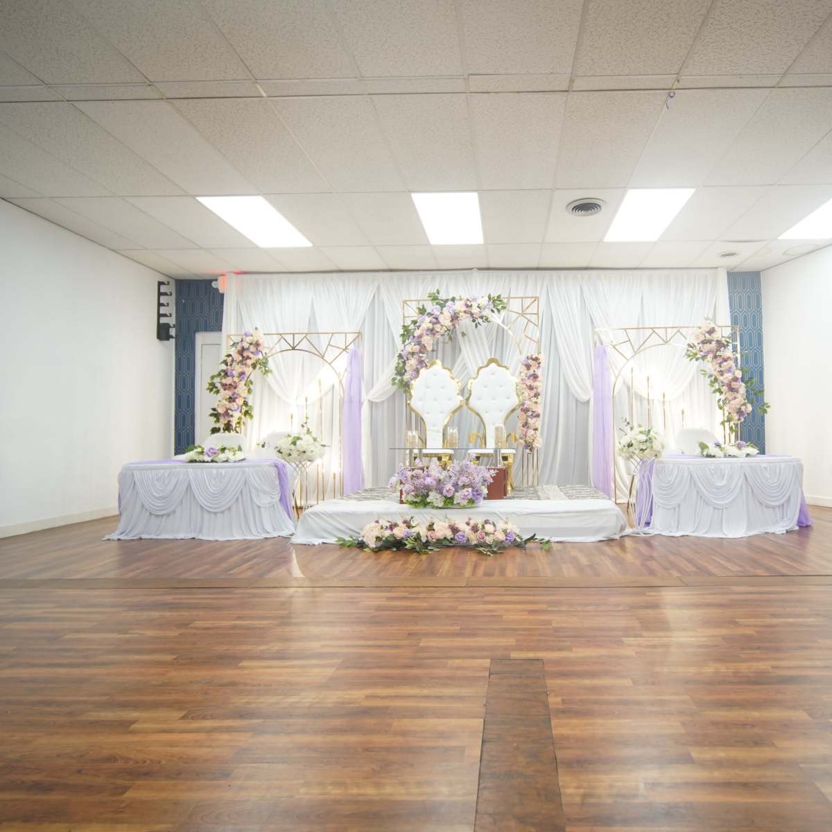 A decorated event space with a floral arrangement and two tables set up on a wooden floor.