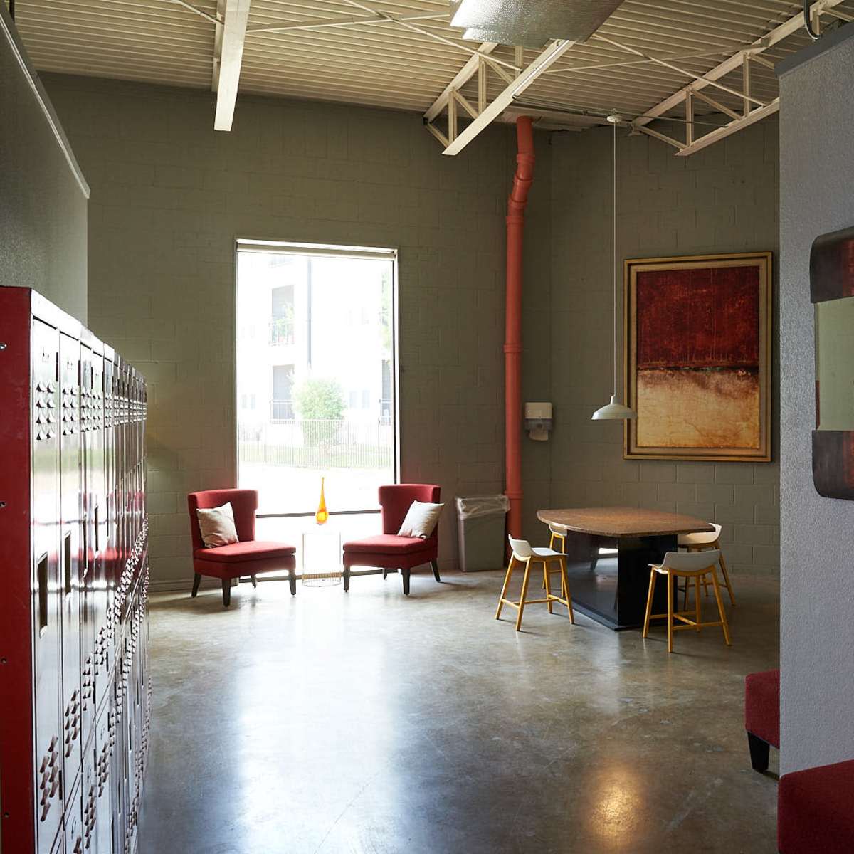 An interior space featuring red lockers, two red chairs, a wooden table with yellow chairs, and a large window.