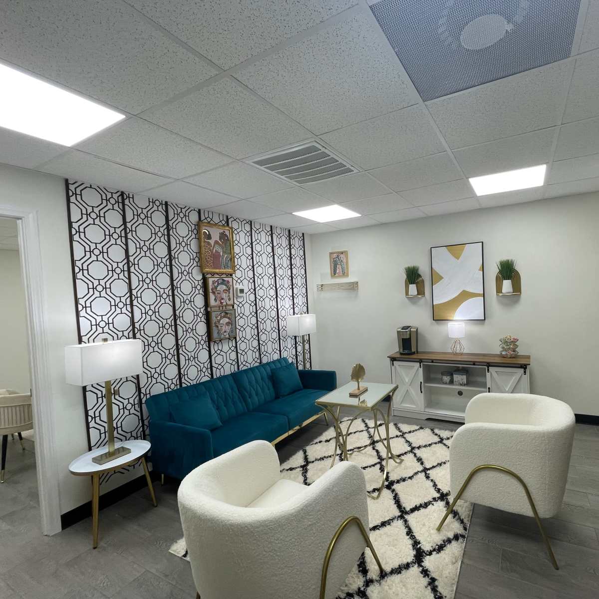 A modern waiting room with a teal sofa, two white armchairs, a coffee table, and decorative wall art.