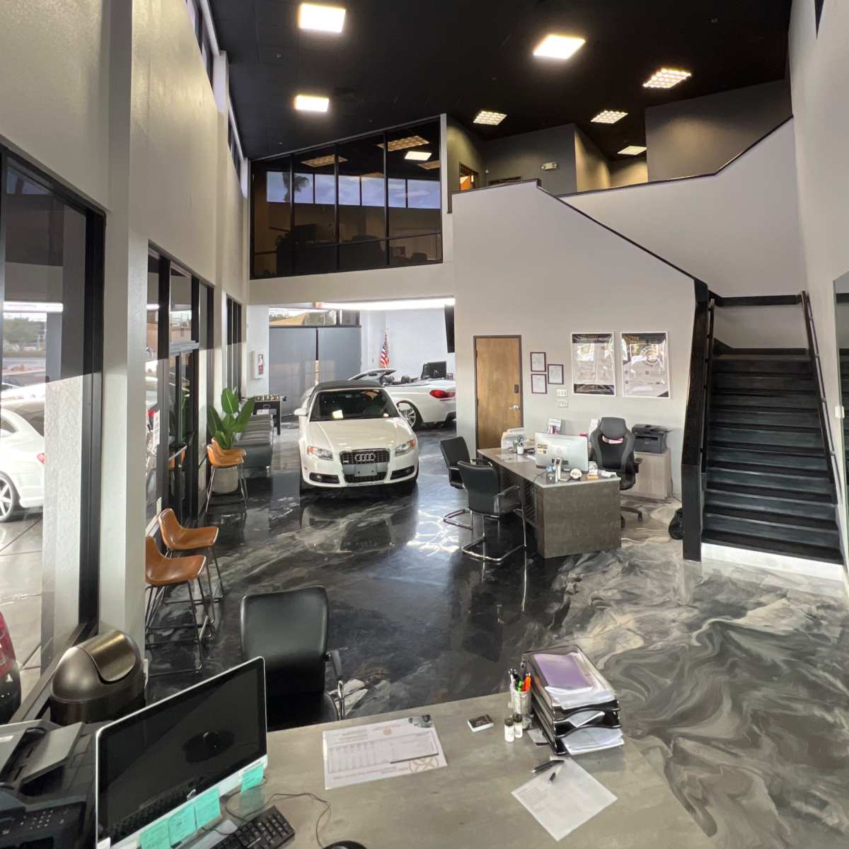 The interior of a car dealership with a sleek, modern design featuring a vehicle on display and a reception area with desks and chairs.