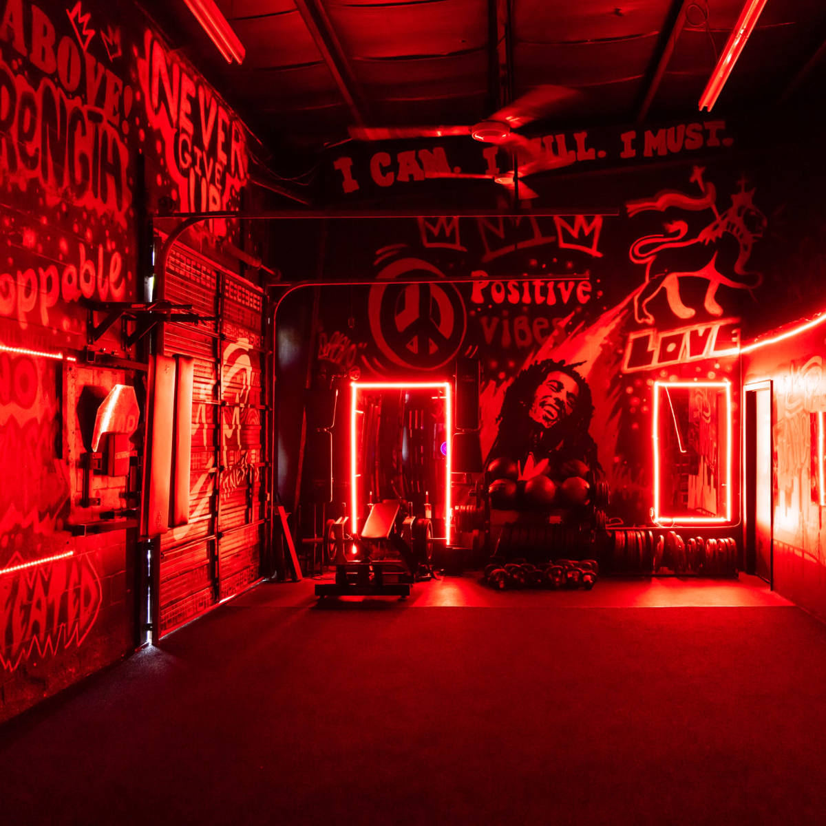 A gym with red neon lighting and vibrant graffiti on the walls, including motivational phrases and a mural of a person.