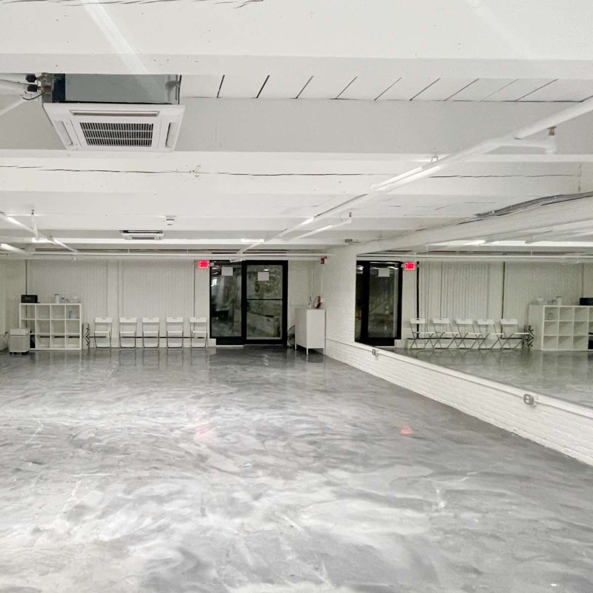 An empty, well-lit studio space with gray flooring and a large mirror on one wall.