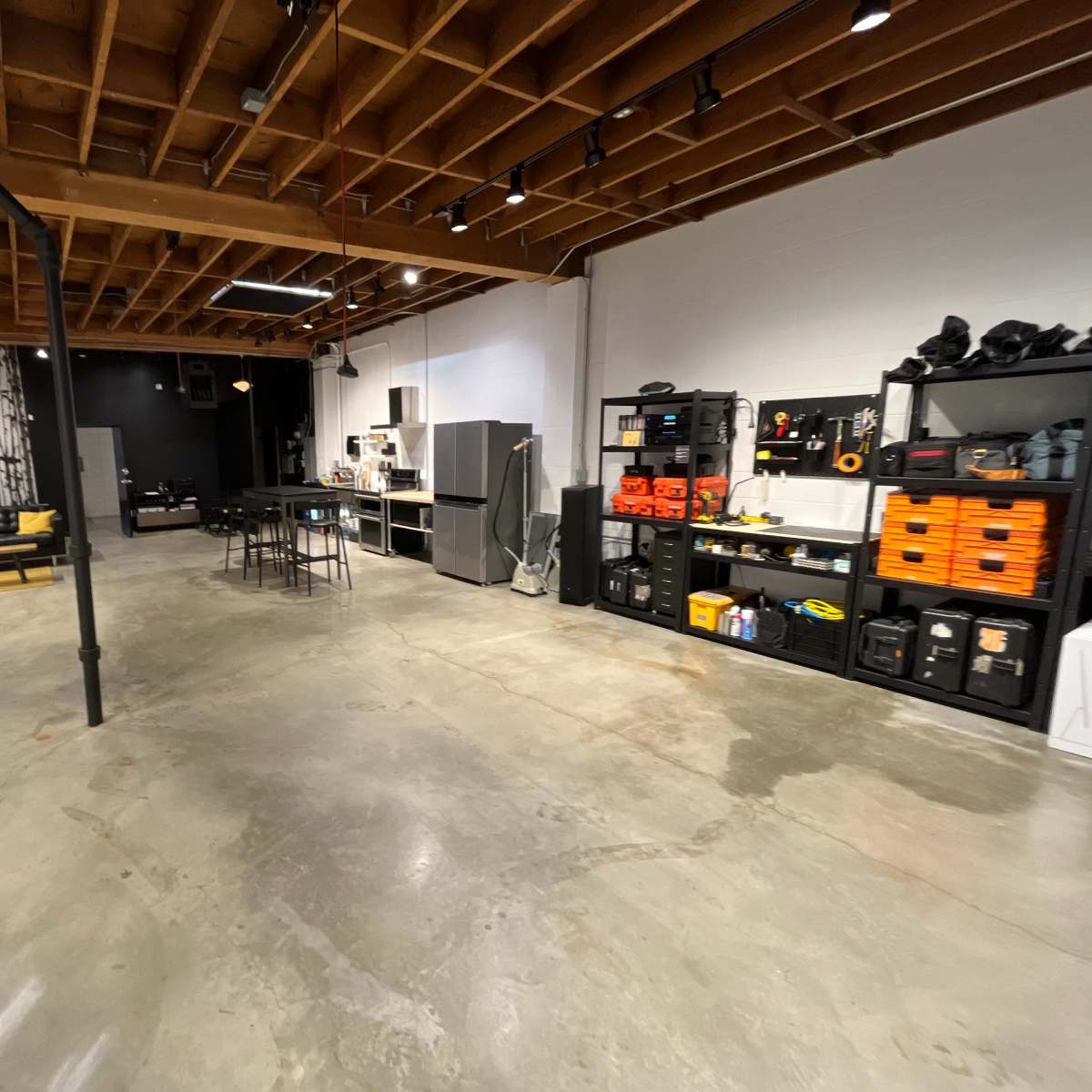 A spacious, industrial-style room with concrete floors, exposed wooden beams, and organized storage on one side.