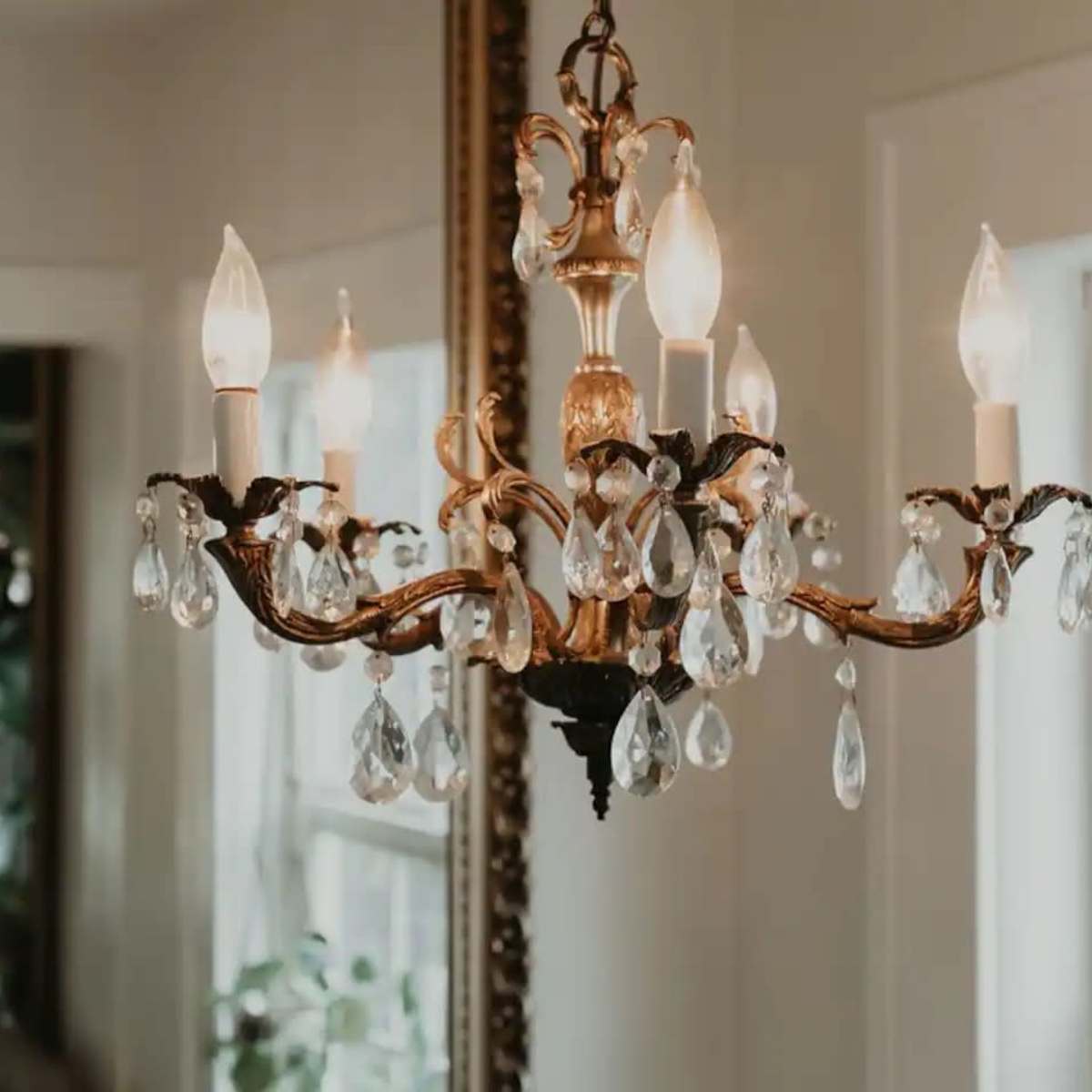 Two ornate chandeliers hanging in a room, with one reflected in a large mirror.