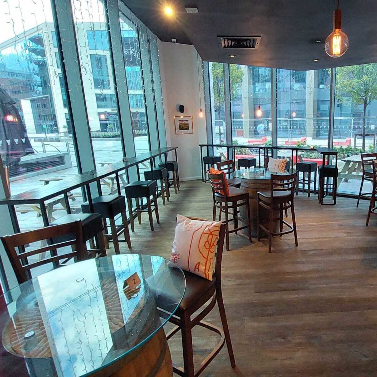 A modern cafe interior with wooden tables and chairs arranged around large windows that face a street.