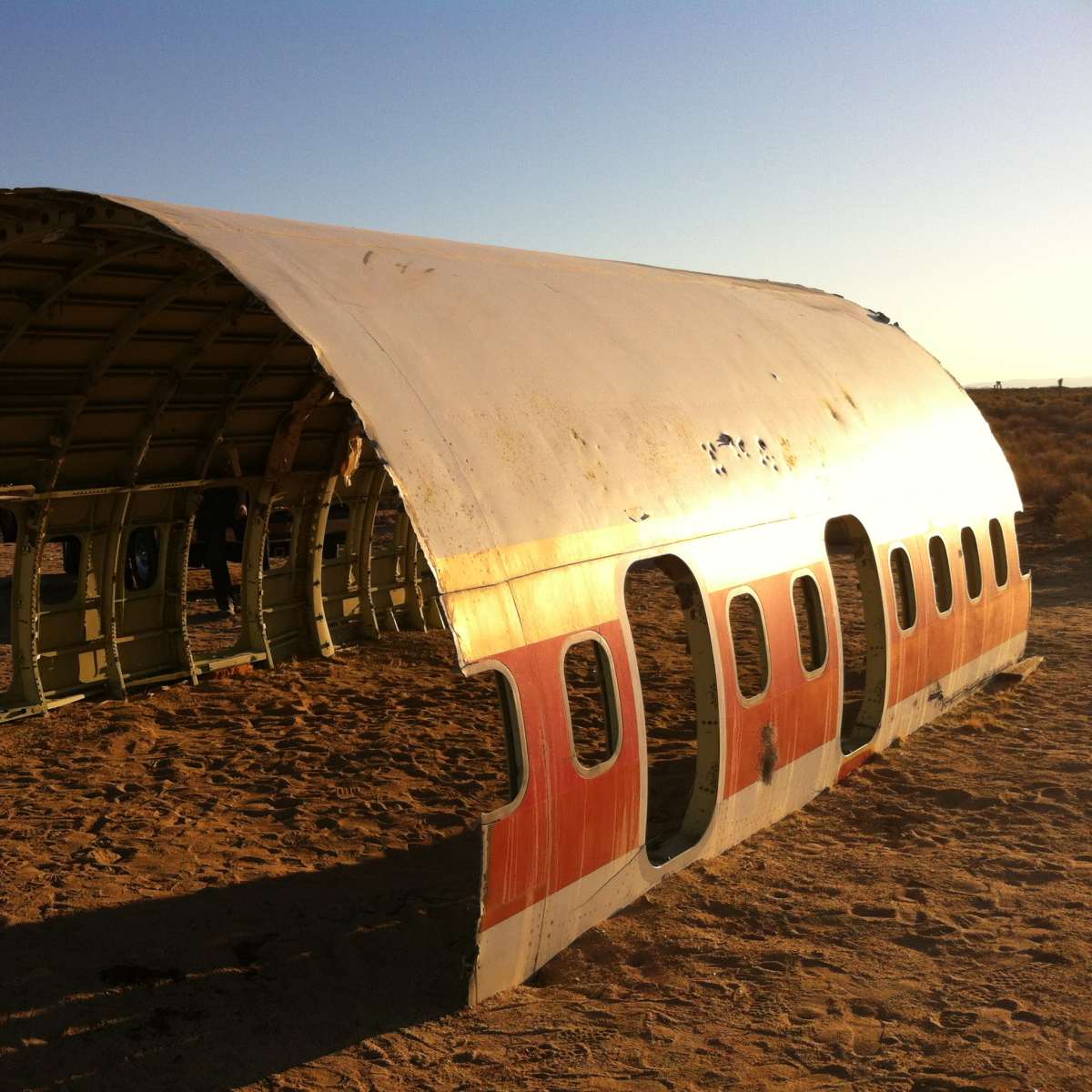 An airplane fuselage sits abandoned in a sandy desert landscape.