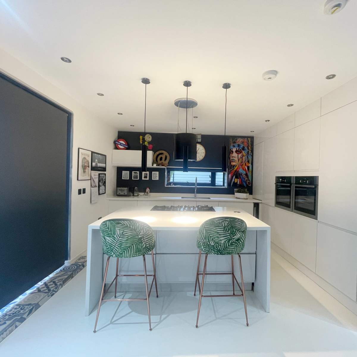 A modern kitchen featuring a central island with two bar stools, sleek cabinetry, and black accents.